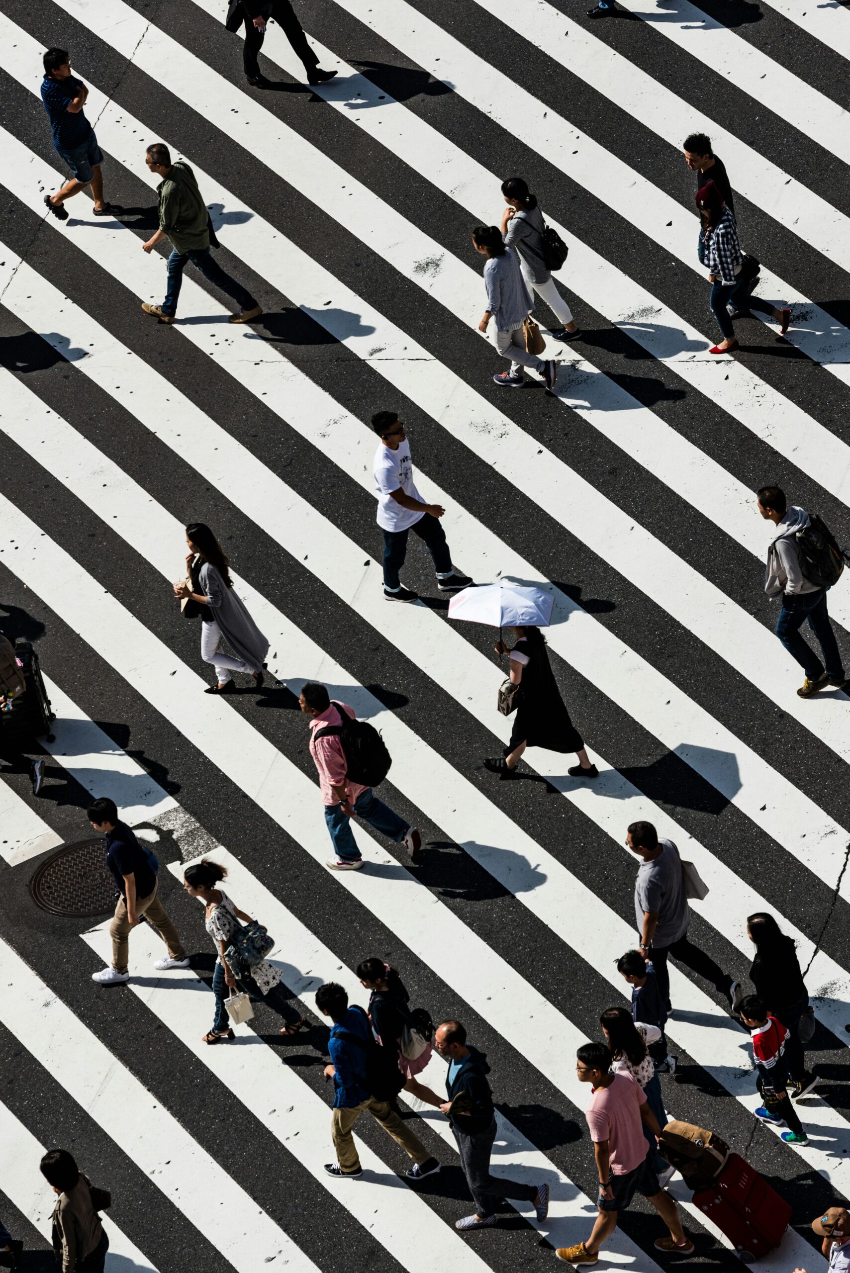 Overhead shot of pedestrians crossing a diagonal striped crosswalk, representing daily leadership flow and urban life -City Boss Coaching-Kellye Mazzoli